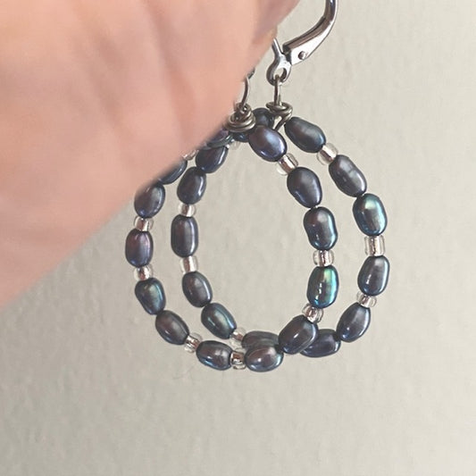 Model's fingers holding grey freshwater pearl teardrop earrings with white seed bead accents