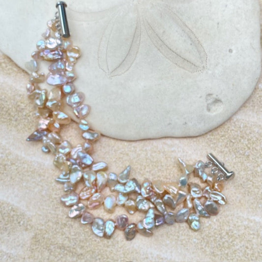 Hand-knotted triple strand pink peach 7-inch keshi pearl bracelet with channel sterling magnetic clasp shown on a sand-dollar prop