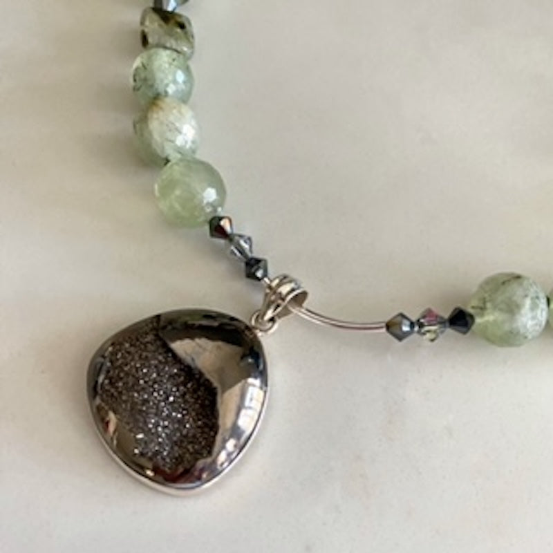 Alternate partial view of the centre Black Drusy moving pendant, sterling curved tube and Prehnite beads at the centre of the 18-inch hand-knotted necklace