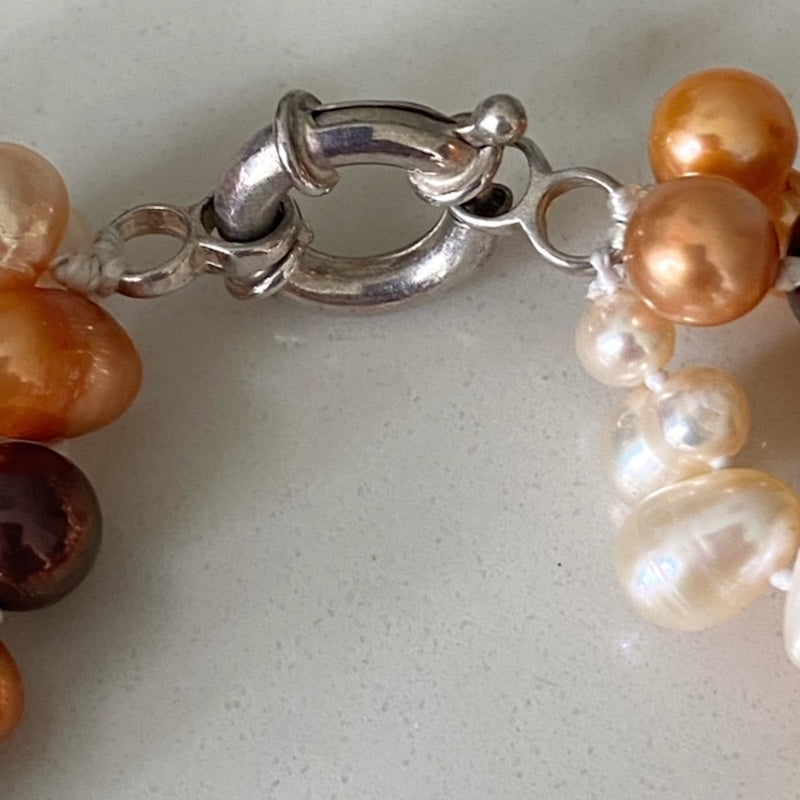 Closeup of metal slip ring clasp of the orange brown white knotted triple strand pearl necklace