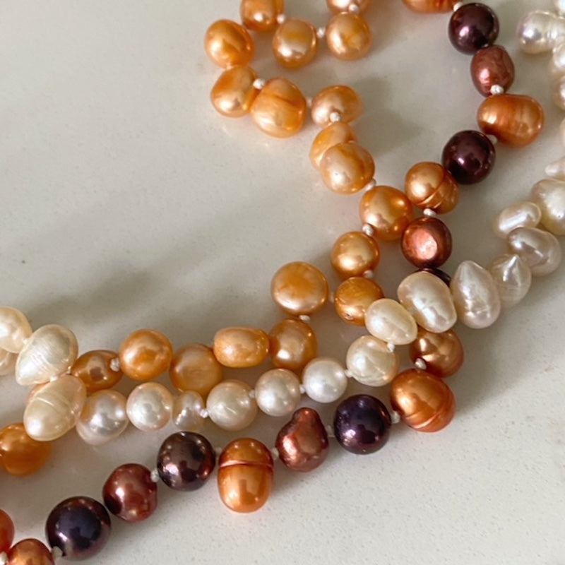 Closeup of the orange brown white knotted pearls of the triple strand necklace