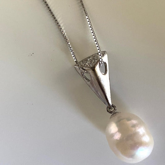 Closeup of the oval creamy white Baroque pearl and its triangle wedge pendant with threaded sterling chain