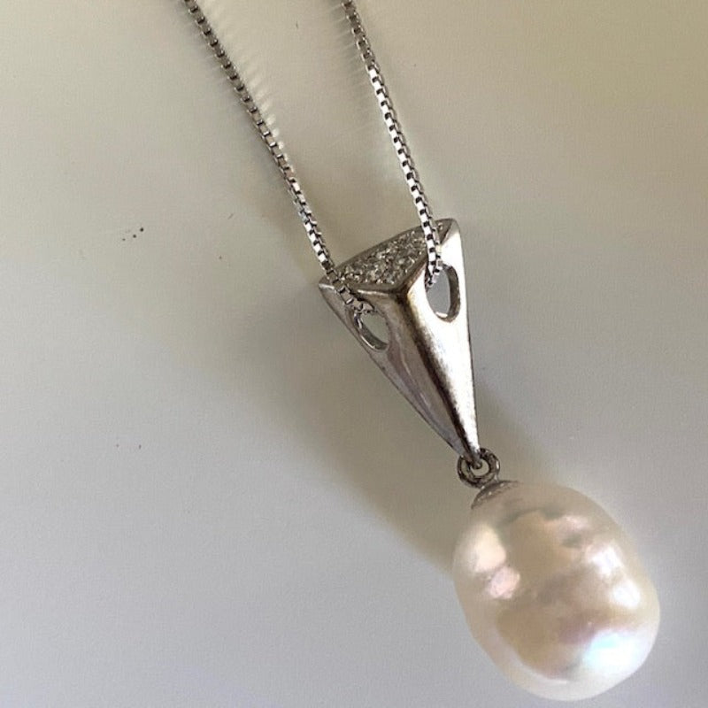 Closeup of the oval creamy white Baroque pearl and its triangle wedge pendant with threaded sterling chain