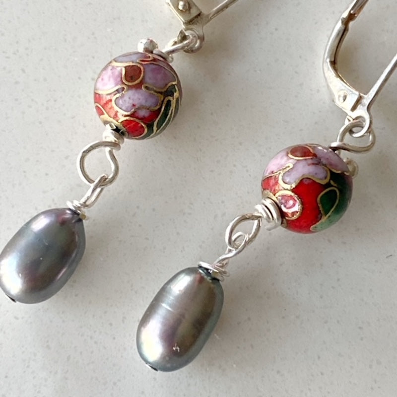 Closeup details of the round red metal cloisonne bead and grey potato freshwater pearls on these dangling 1-inch earrings