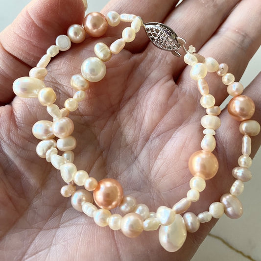 Double strand creamy white and golden-peach freshwater pearl 7-inch bracelet shown on the palm of a model