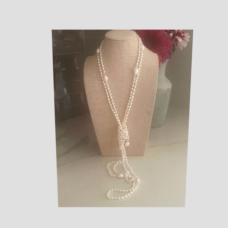 Front view of the super long 96-inch pearl necklace double draped and tied in a loose front knot on linen jewelry stand in front of flowers