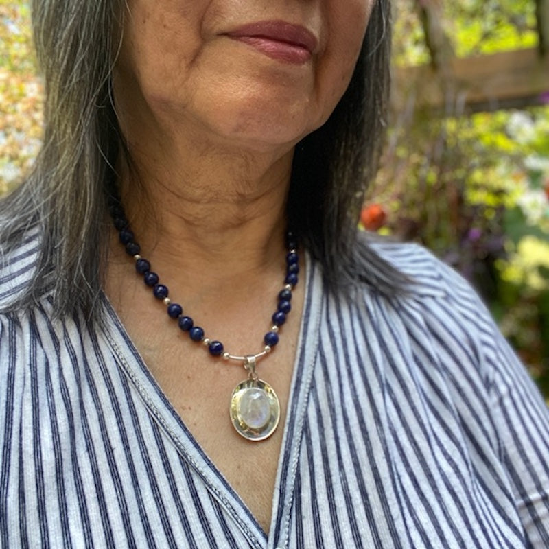 Closeup of model in a striped blue top wearing the Lapis Moonstone Kinetic Motion Necklace outside