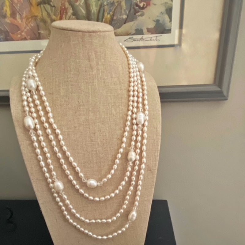 Super long 96-inch knotted white pearl necklace on display stand near a painting