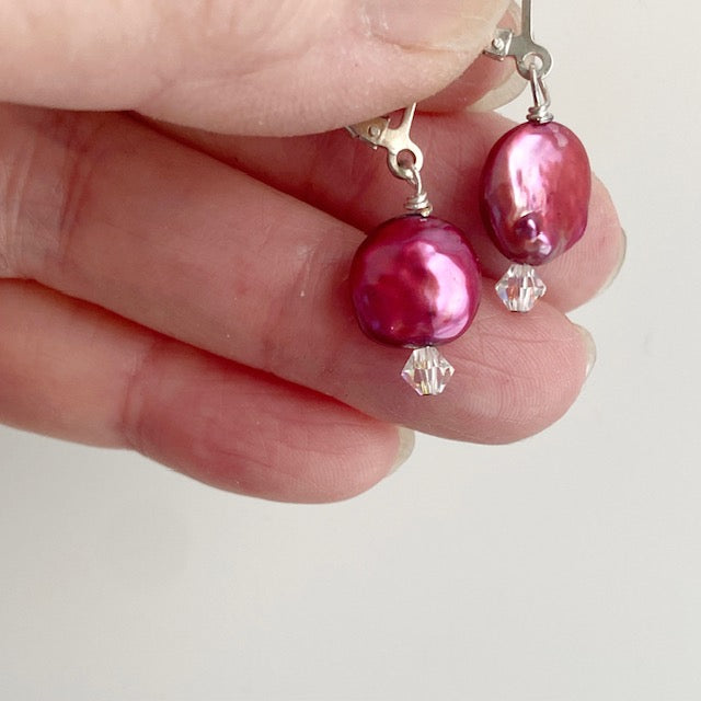 Lever-back cranberry-coloured dyed coin pearl earring shown held on model's fingers