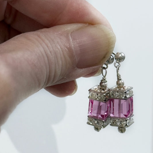 Pink gemstone earrings held by a hand against a white background