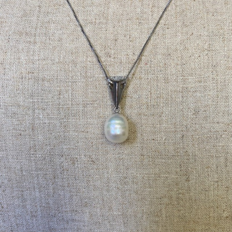 Closeup of oval creamy white baroque pearl sterling triangle wedge pendant on linen background