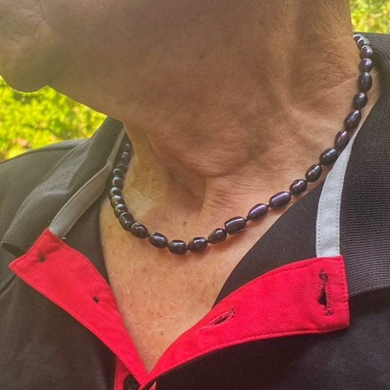 Side view of male model wearing unisex black pearl 18-inch knotted necklace