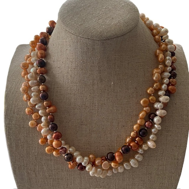 Triple strand orange brown white knotted pearl necklace shown on linen display stand