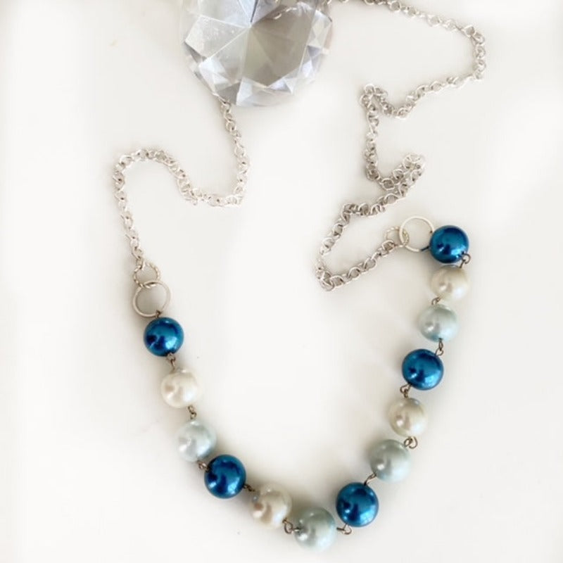 Wire-wrapped blue and white 30-inch faux shell pearl necklace with silver-plated chain top view shown with jewelry gem diamond prop 