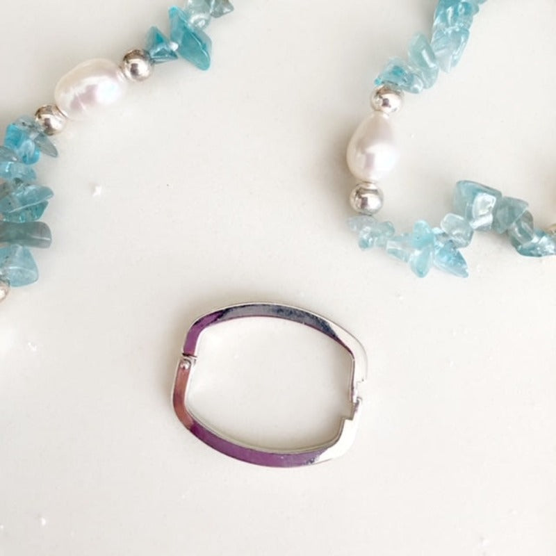 Closeup view of the silver-plated link clasp  and partial view of the aquamarine chip white pearl necklace