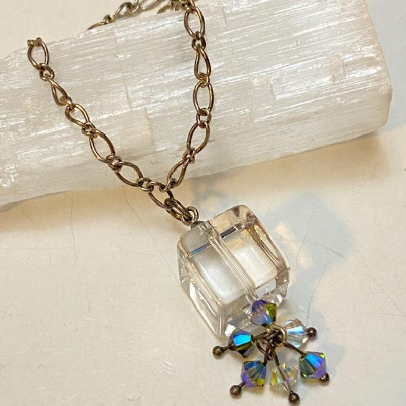 Clear cube pendant necklace with sparkling blue-green  and white crystal accents shown propped against a Selenite bar