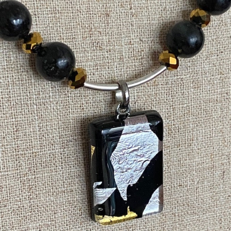 Closeup dichroic black-silver-gold pendant on sterling tube  of the hand-knotted granite, gold crystal, black onyx necklace