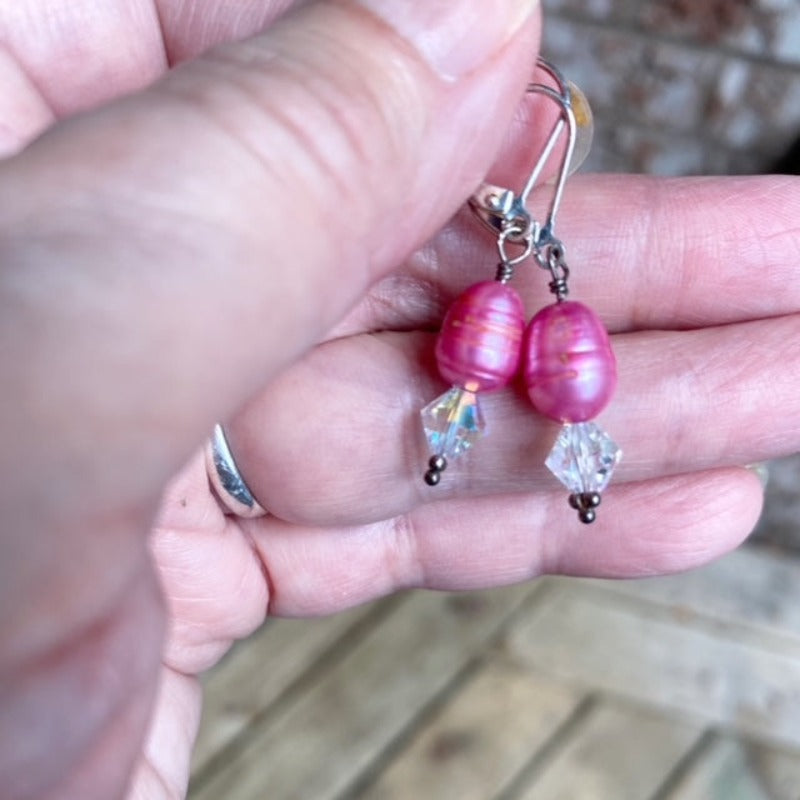 Model holding the pair of dyed bright pink pearl and sparkling white Austrian crystal lever-back earrings