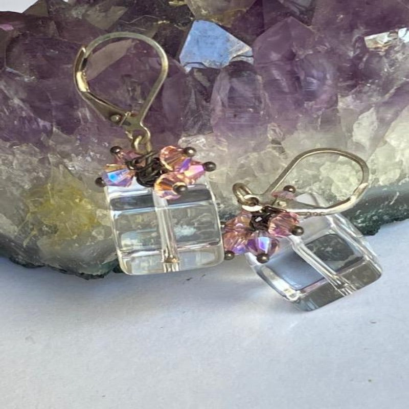 Sparkling clear cube bead with wire-wrapped pink mini crystals topping it like a present on sterling lever back ear wires shown propped against Amethyst display