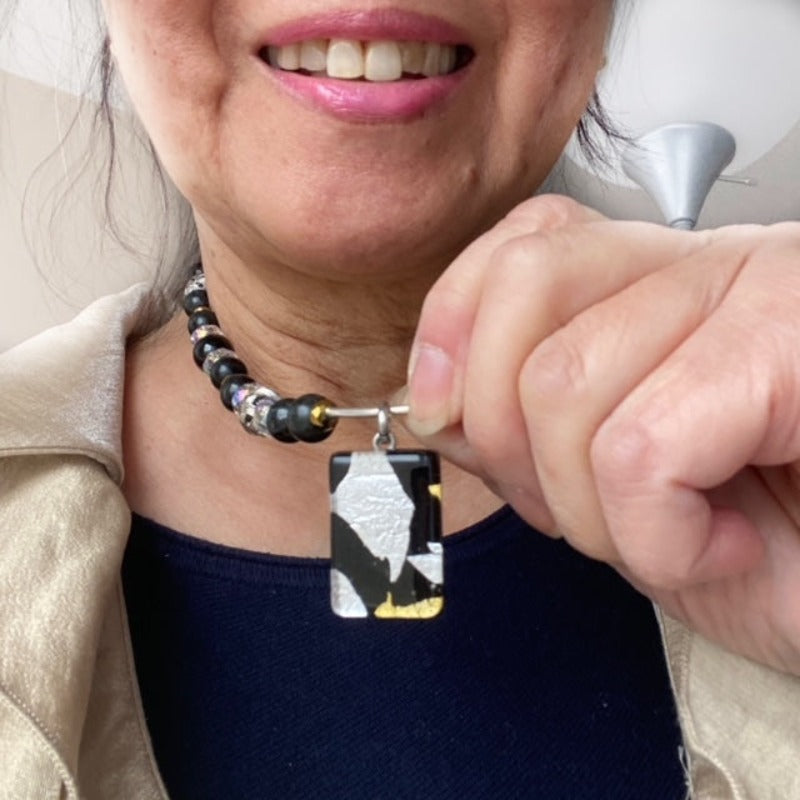 Model holding up the dichroic black-silver-gold glass pendant on the Sterling silver tube