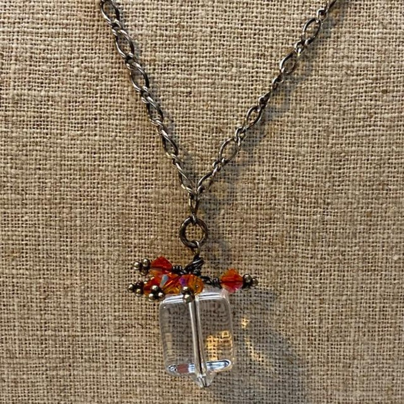 Clear cube pendant topped with orange Austrian crystals to resemble a present with bow shown on linen bust