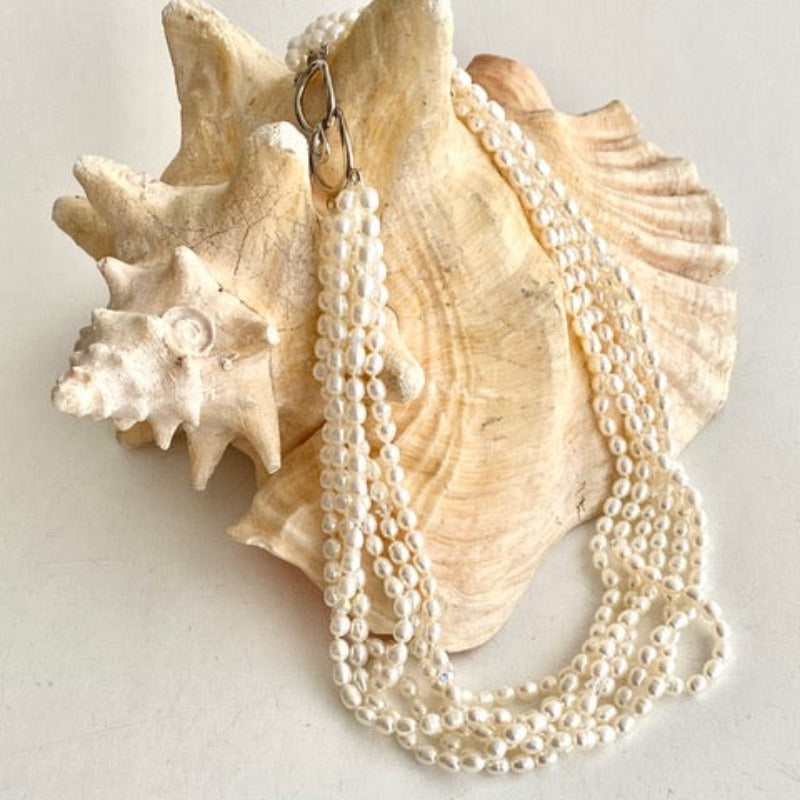 Six strand knotted white pearl with accent crystals and easy hook together clasp shown draped on a conch shell prop