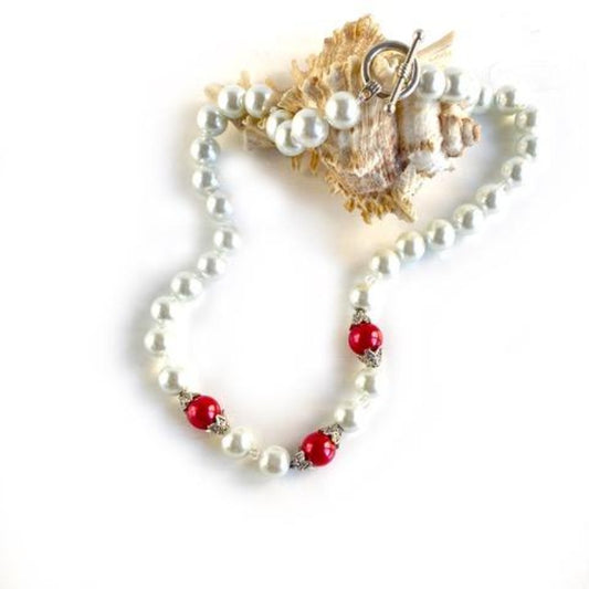 White and red faux pearl hand-knotted necklace shown top view on shell display